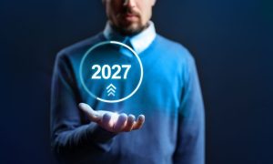Man Wearing Blue Sweater with Digital Image Of 2027 Inside Circle Hovering Over His Open Palm