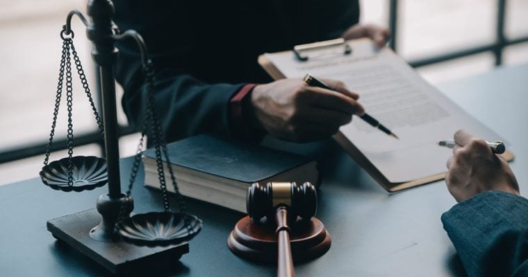 Two Men Review Legal Document With Judges Gavel and Scale on Desk