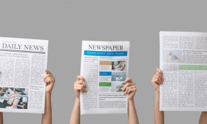 Three Hands Hold Newspapers Up Above Heads on Solid Gray Background