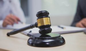 Two People Sit At Desk Reviewing Legal Documents with Black and Gold Judge's Gavel in Foreground