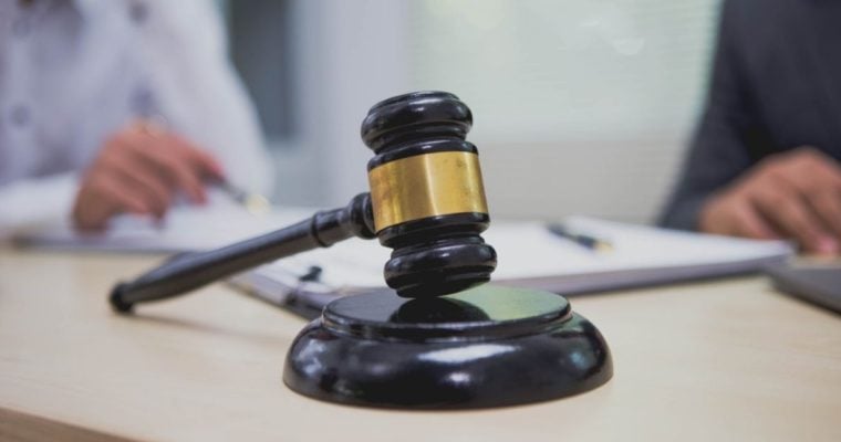 Two People Sit At Desk Reviewing Legal Documents with Black and Gold Judge's Gavel in Foreground