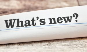 Rolled Up Newspaper on Wood Table Reads What's New?