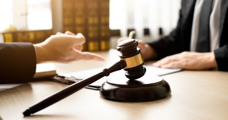 Judge's Gavel Sits on Lawyer's Desk As They Discuss With Client