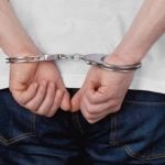 Man in White T-Shirt and Blue Jeans Has Hands in Handcuffs