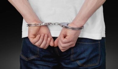 Man in White T-Shirt and Blue Jeans Has Hands in Handcuffs