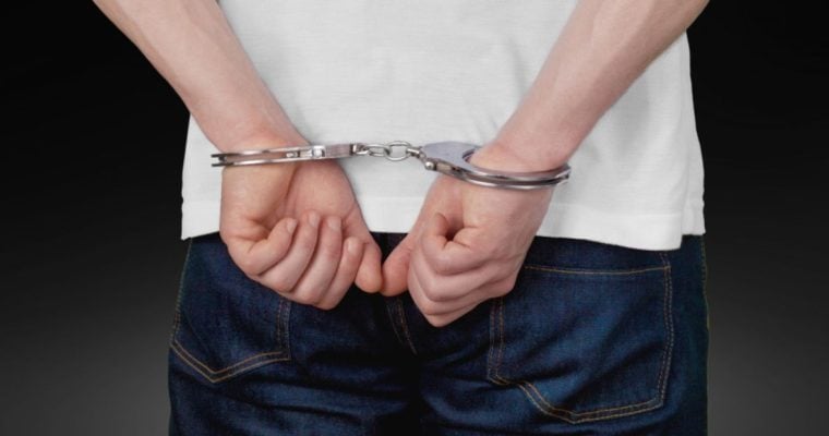 Man in White T-Shirt and Blue Jeans Has Hands in Handcuffs