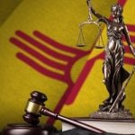 Yellow and Red State Flag of New Mexico, Background to Metal Statue of Lady Justice Sitting on Book