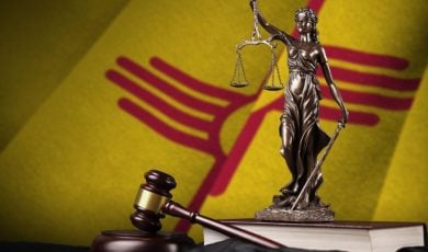 Yellow and Red State Flag of New Mexico, Background to Metal Statue of Lady Justice Sitting on Book