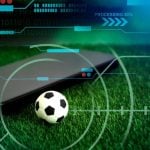 Green Grass with Mini Soccer Ball and Black Cell Phone in Sports Betting Concept