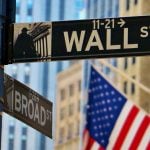 NYC Buildings and American Flag Hangs in the Background of Wall Street Sign