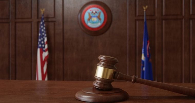 Judge's Gavel Sits on Wooden Desk Inside Courtroom with Michigan & US Flag Background
