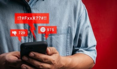 Man in Denim Shirt Holds Cell Phone Displaying Negative Comments in Red