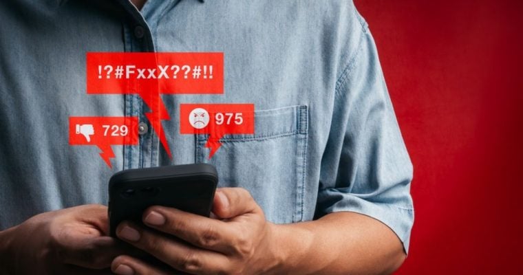 Man in Denim Shirt Holds Cell Phone Displaying Negative Comments in Red