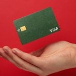 Cupped Hand with Green Visa Card Hovering Above it on Red Background