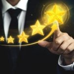 Man in Black Suit and Tie Points to Biggest Gold Star out of 5