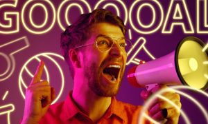 Neon Letters Spell GOAL with Whistle and Soccer Ball Behind Man Yelling in Megaphone