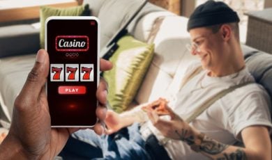 Happy Man with Tattoos Sits On Couch and Cell Phone Displaying Online Casino in Foreground