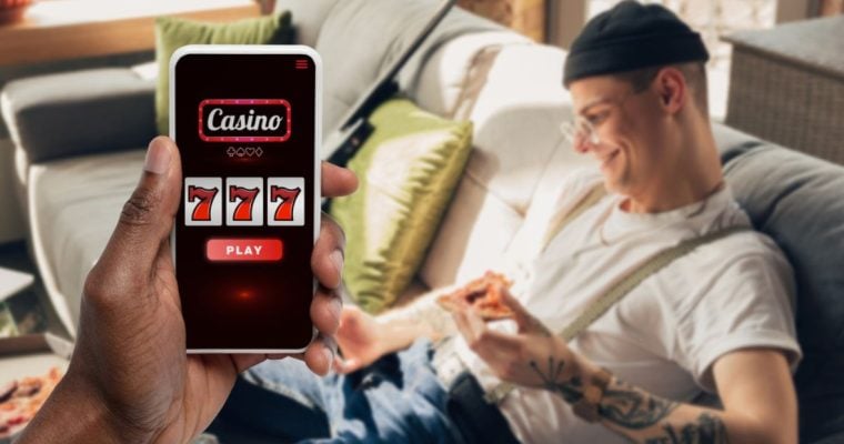 Happy Man with Tattoos Sits On Couch and Cell Phone Displaying Online Casino in Foreground