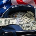 Bag Full of $100 American Banknotes Sit on Top of American Flag