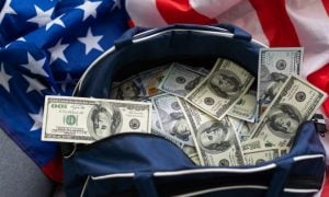 Bag Full of $100 American Banknotes Sit on Top of American Flag
