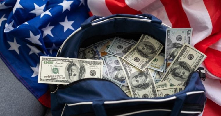 Bag Full of $100 American Banknotes Sit on Top of American Flag