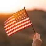 Pink and Yellow Sunset Light Shines Through American Flag in Someone's Hand