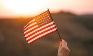 Pink and Yellow Sunset Light Shines Through American Flag in Someone's Hand