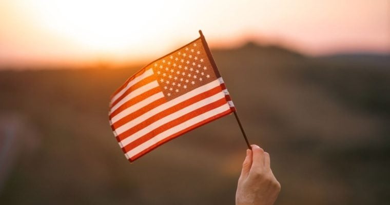 Pink and Yellow Sunset Light Shines Through American Flag in Someone's Hand
