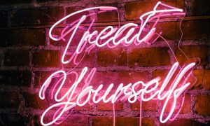 Hot Pink Neon Sign Hanging on Red Brick Wall Reads Treat Yourself