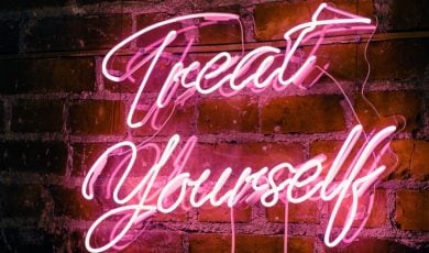 Hot Pink Neon Sign Hanging on Red Brick Wall Reads Treat Yourself