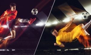 Two Young Male Soccer Players Mid-Air Kicking Ball Inside Stadium