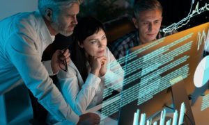 Three People Stare at Computer Monitor with Digital Image Overlay of Data and Charts