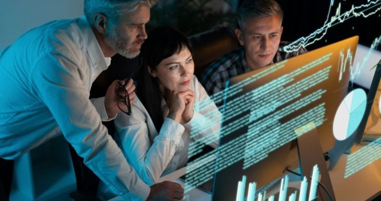 Three People Stare at Computer Monitor with Digital Image Overlay of Data and Charts