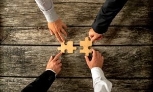 Four successful business men joining two puzzle pieces each bein