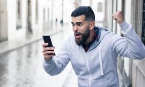Enthusiastic,Young,Man,Looking,At,Cellphone,With,Victorious,Expression,In